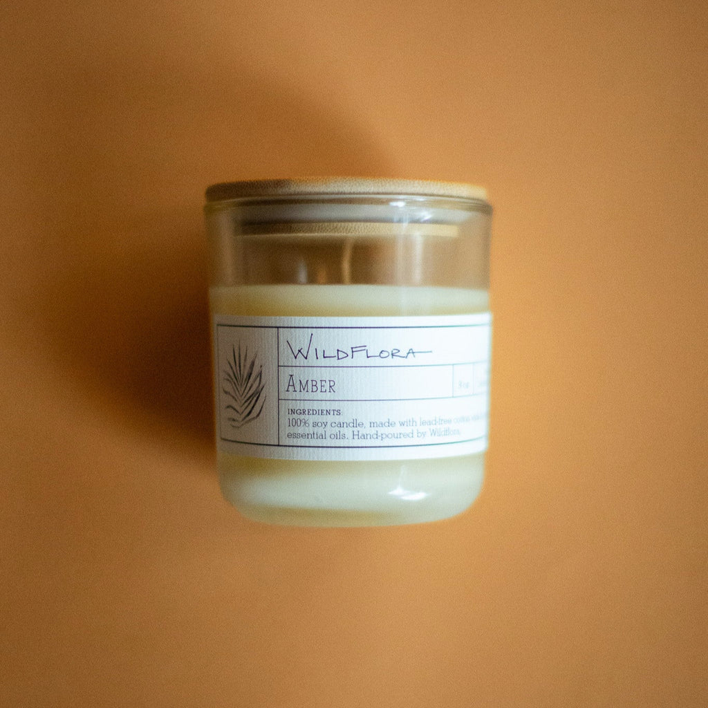 WildFlora Amber Candle in a glass jar with a label on an orange background