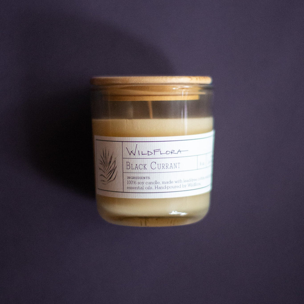 WildFlora Black Currant Candle with a wooden lid on a dark purple background