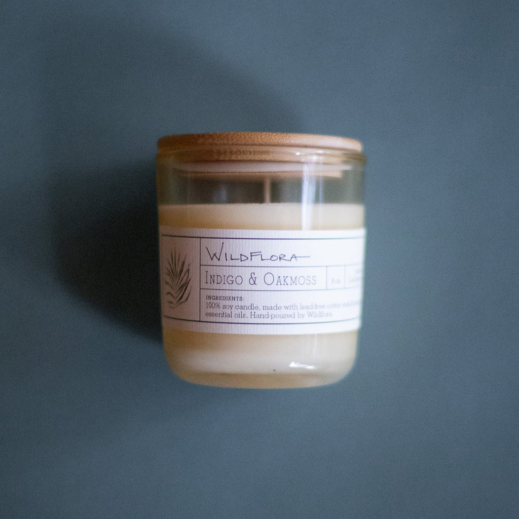 WildFlora Indigo & Oakmoss Candle with wooden lid and white label on a dark background