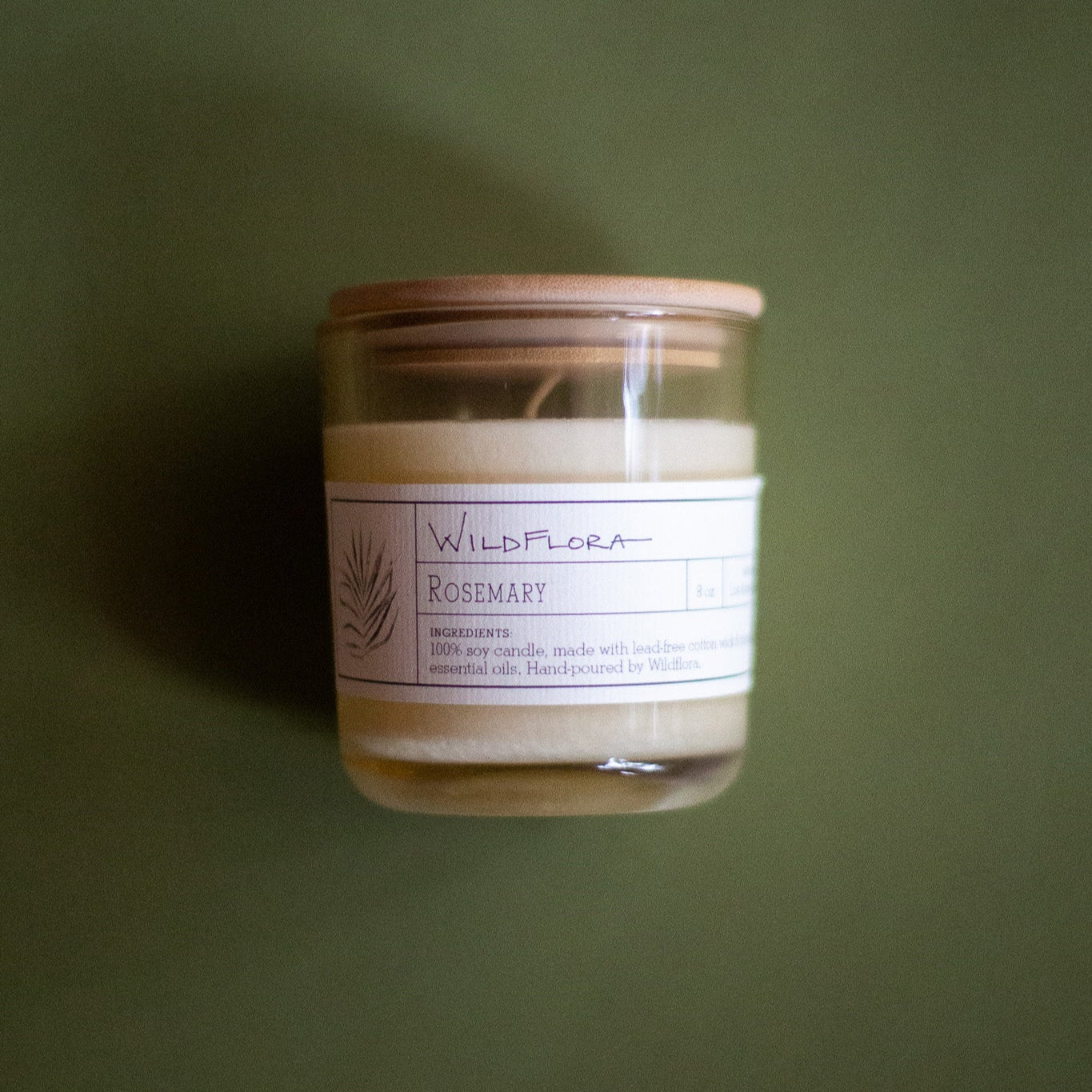 WildFlora Rosemary Candle jar with a label and wood lid on a green background