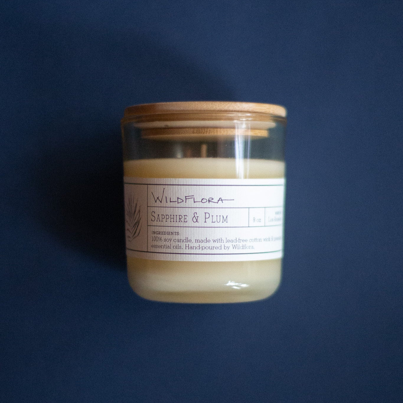 WildFlora Sapphire & Plum Candle with a wooden lid on a dark blue background
