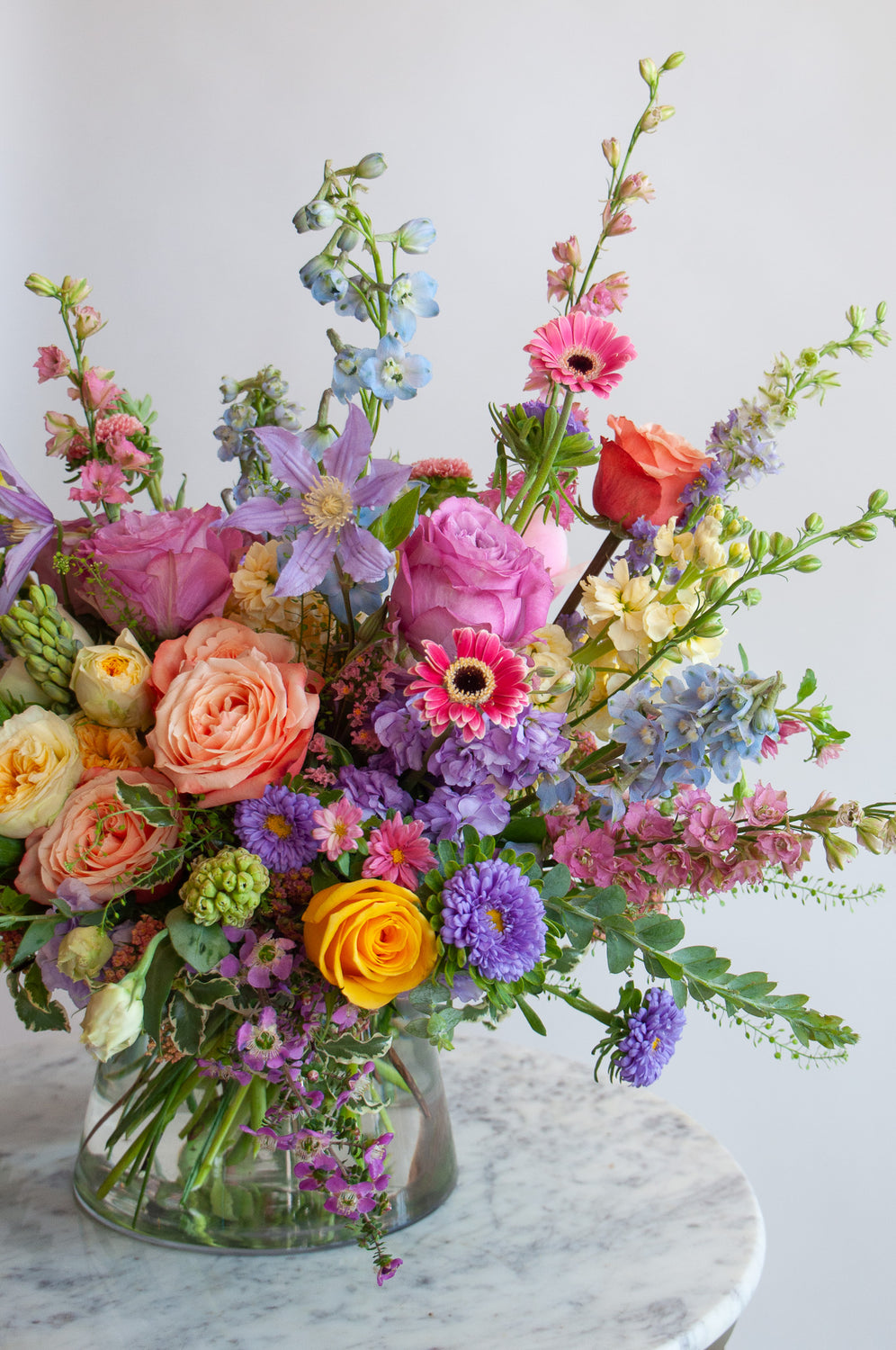 Close up of the blooms in a flower arrangement. The flowers are many colors and include roses, tulips, daisies, snapdragon, clematis, stock, hyacinth, and delphinium.