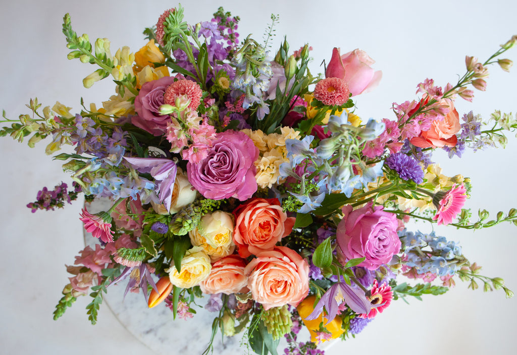 Close up of the blooms in a flower arrangement. The flowers are many colors and include roses, tulips, daisies, snapdragon, clematis, stock, hyacinth, and delphinium.