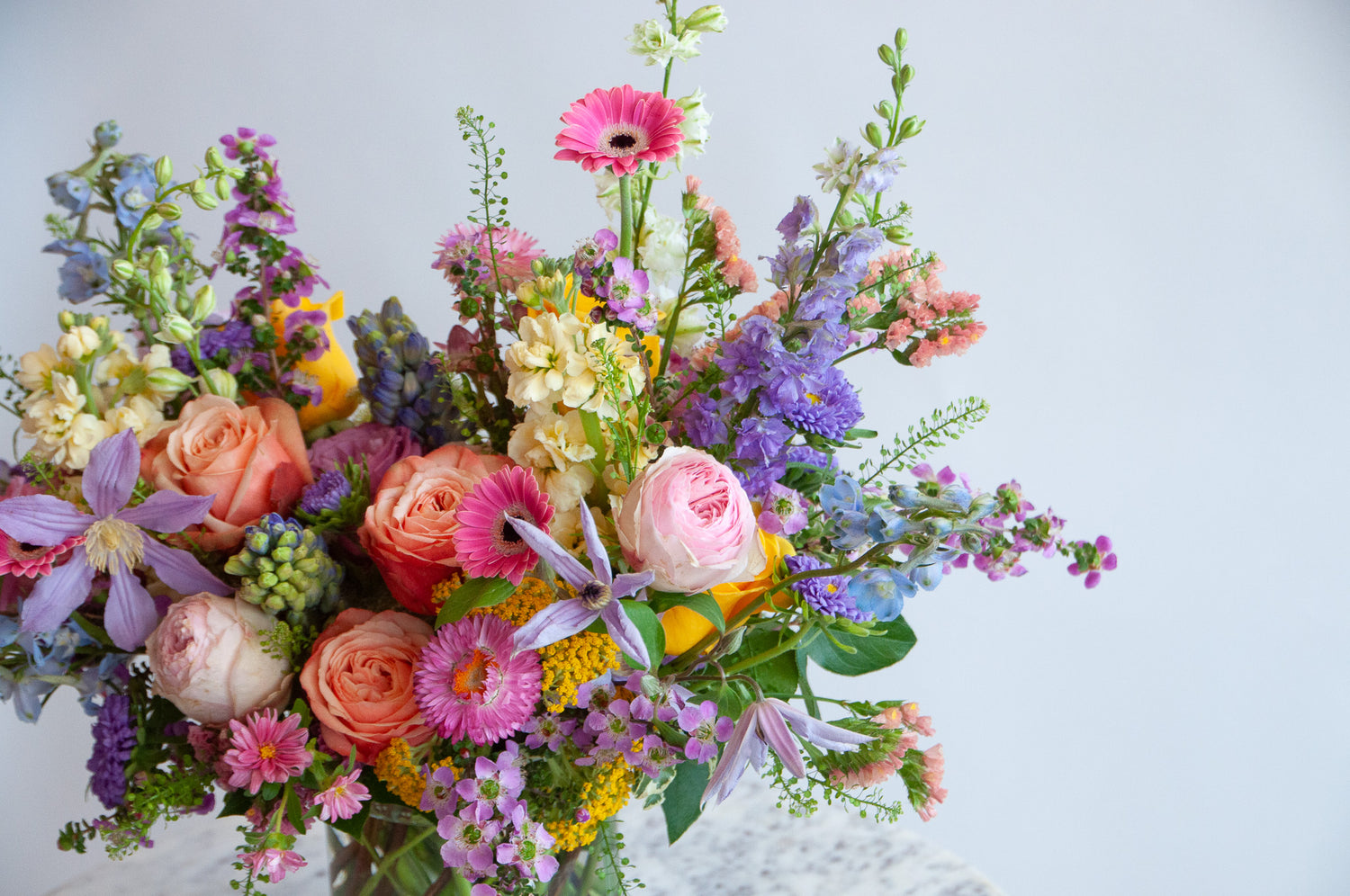 Close up of the blooms in a flower arrangement. The flowers are many colors and include roses, tulips, daisies, snapdragon, clematis, stock, straw flower, and delphinium.