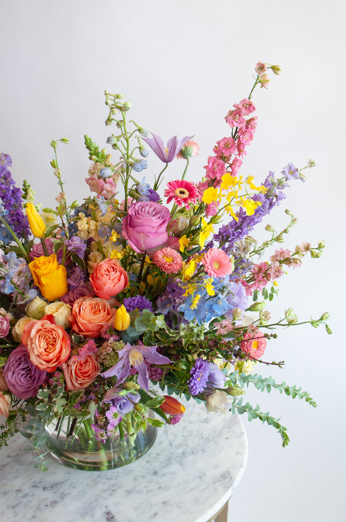 Close up of the blooms in a flower arrangement. The flowers are many colors and include roses, tulips, daisies, snapdragon, clematis, stock, hyacinth, orchids, and delphinium.
