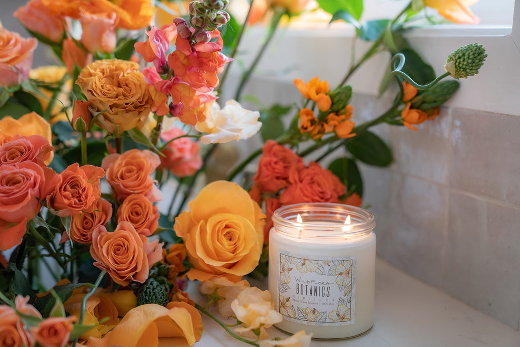 Bouquet of colorful flowers with a lit WildFlora double wick candle on a windowsill