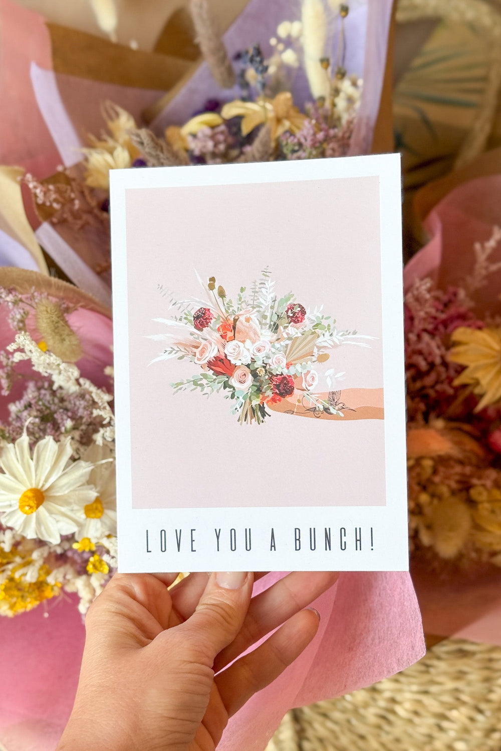 Hand holding a card with floral design and 'Love You A Bunch!' text, surrounded by flowers.