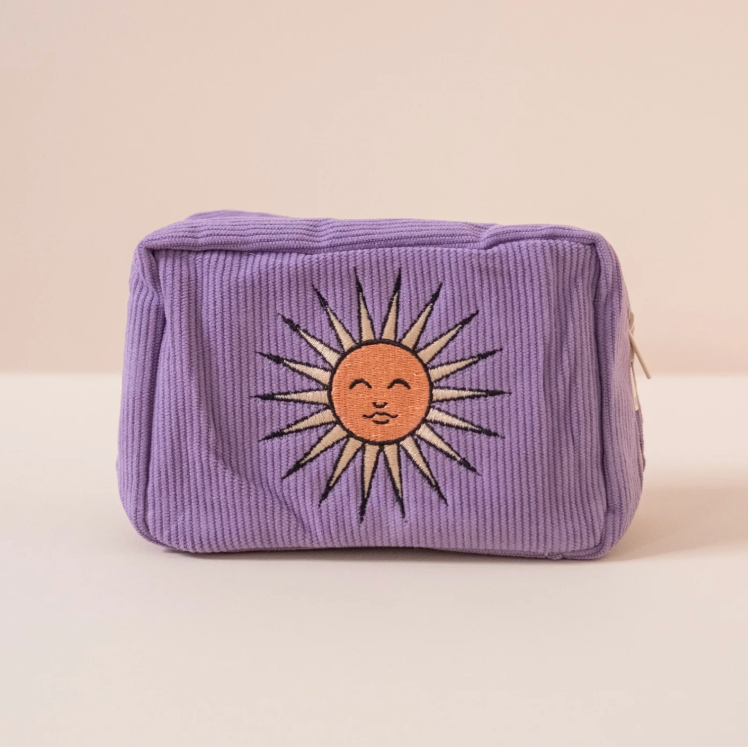 Purple corduroy pouch with a sun design on a beige background