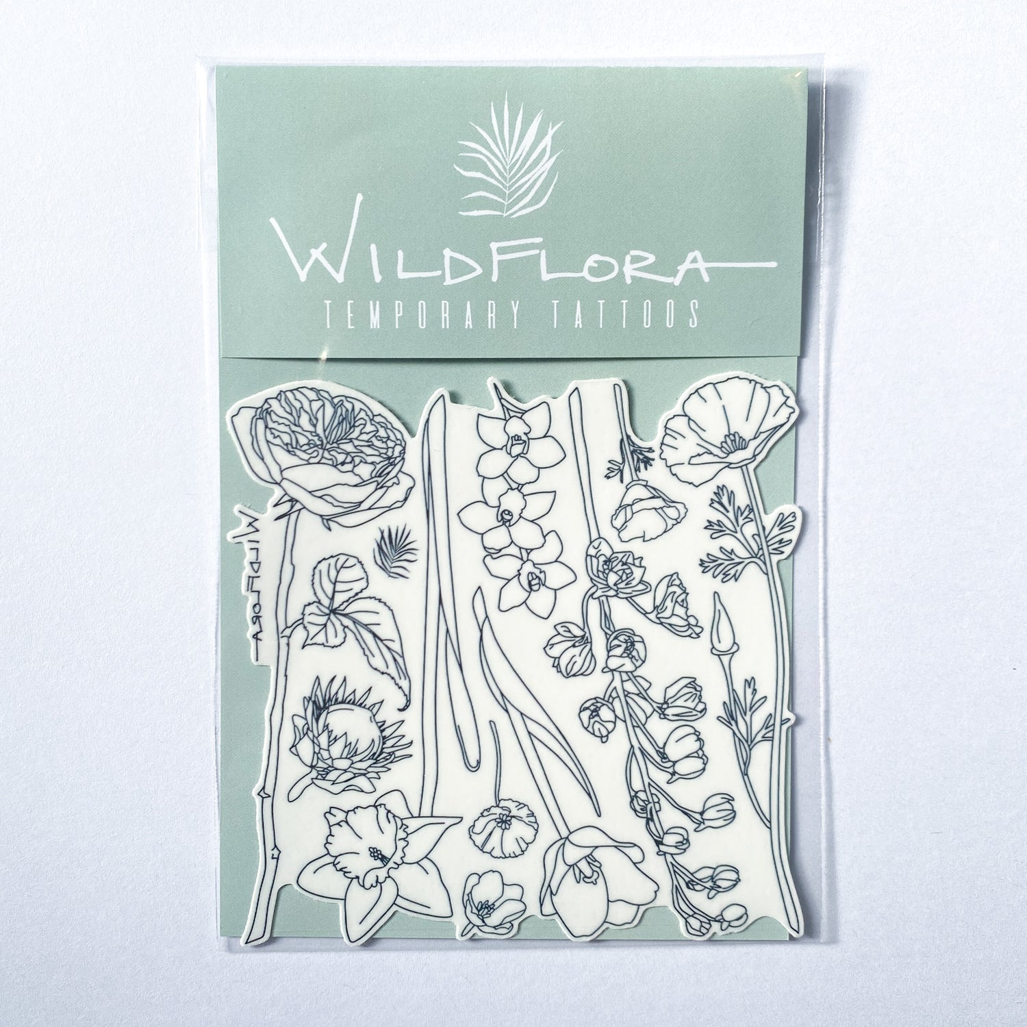 A package of temporary tattoos that are black line drawings of varying flowers, including rose, protea, daffodil, california poppy, tulip, orchid, and delphinium.